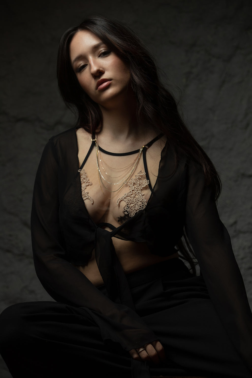 Woman wearing a black lace top and sheer black fabric against a dark background