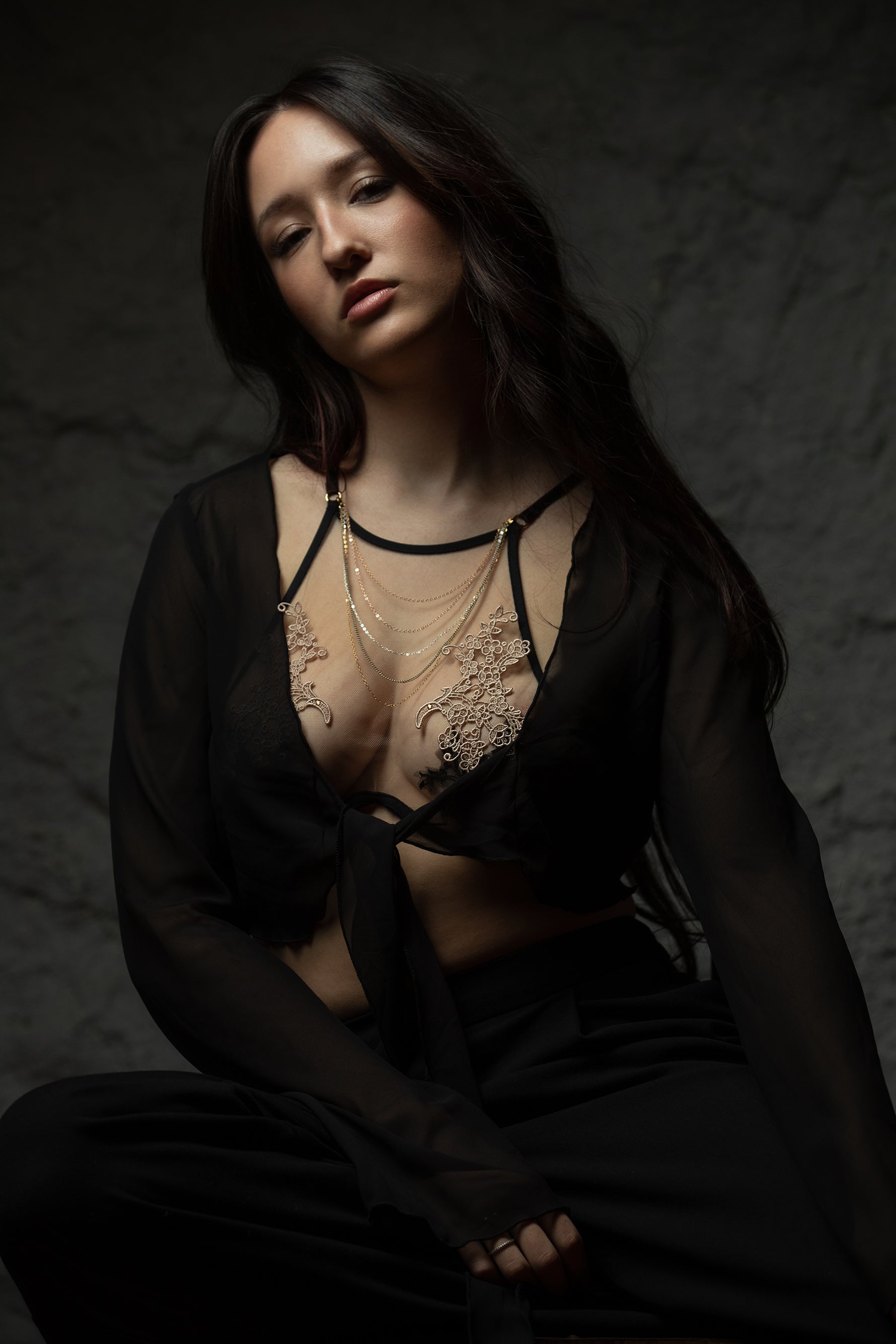 Woman wearing a black lace top and sheer black fabric against a dark background
